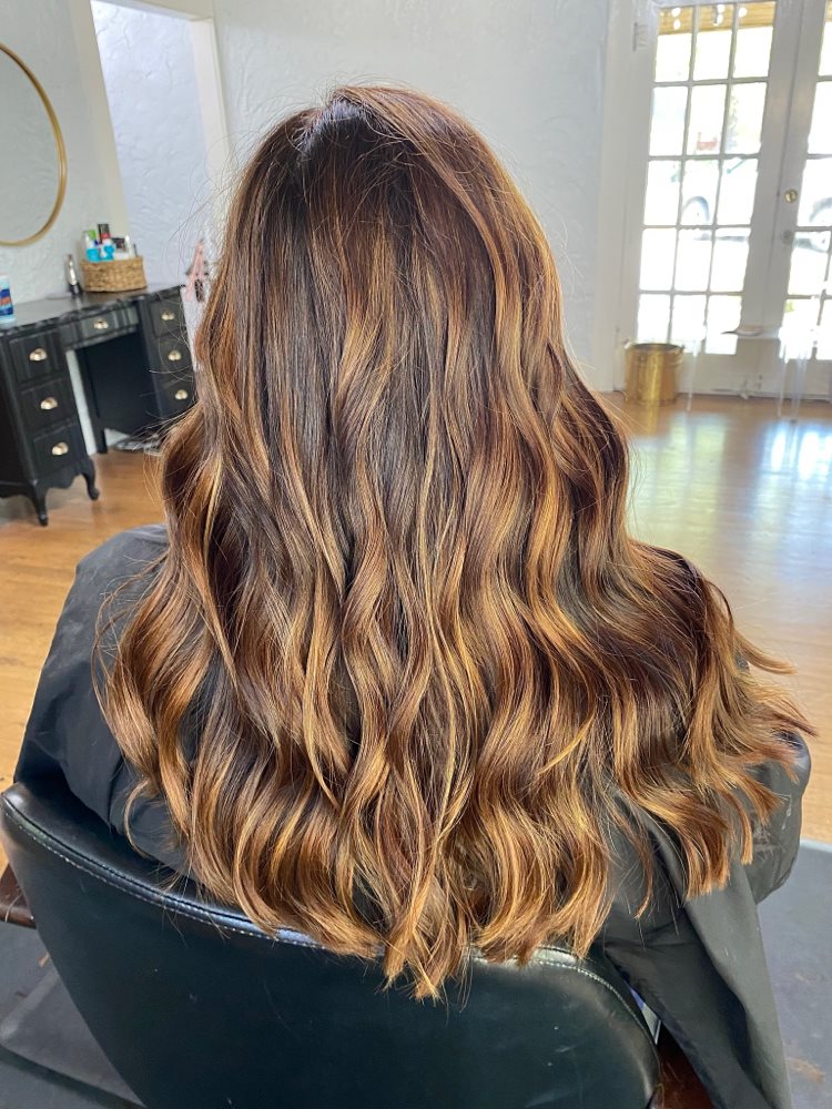 Long brown waves with golden highlights, pictured on Hailey Allen’s balayage service listing.